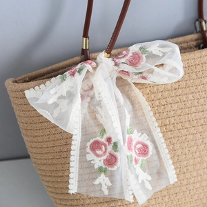 Detailed shot of straw tote bag with lace bow and pink flower embroidery detail