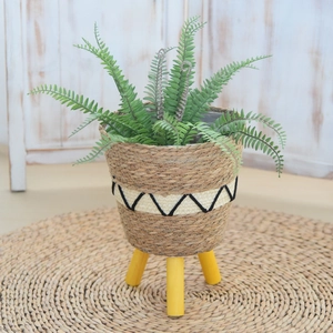 Detail of woven straw plant stand with geometric patterns and yellow wooden legs