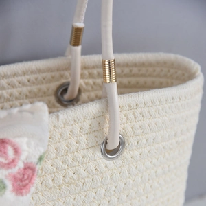 Detail of woven straw tote with leather handle, metal rings and floral embroidery
