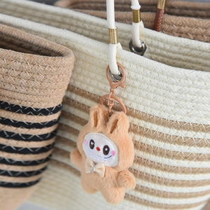 Detail of cute beige plush rabbit keychain charm with bow on a woven tote bag
