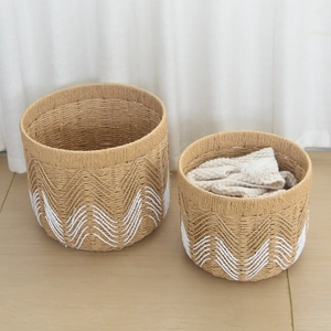 Close-up of two-tone woven cotton storage baskets on light wood floor with soft white curtains