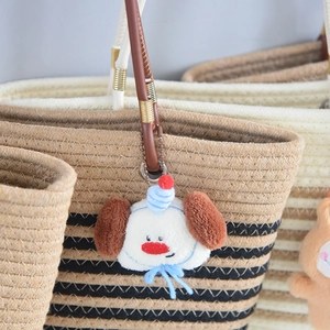 Close-up of a plush dog bag charm with blue tassels hanging on a straw tote handle