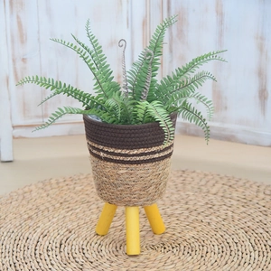 Detail of Nordic woven straw planter with yellow wooden tripod legs and fern plant