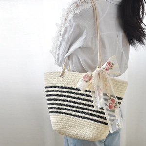 Detail of woven straw tote bag featuring black stripes and a large lace floral bow