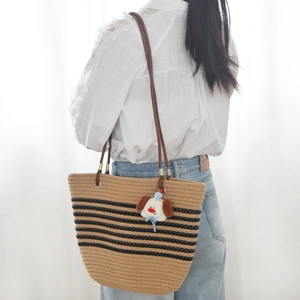 Detail of woven straw tote bag featuring black stripes and a cute plush dog pendant charm