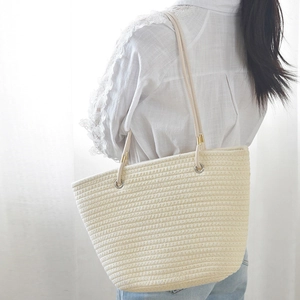 Close-up of cream woven straw tote bag with shoulder straps worn by model