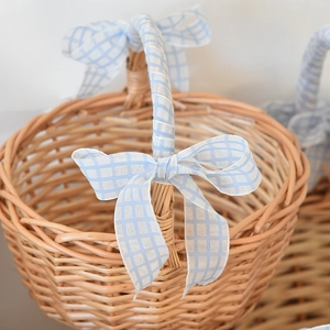 Close-up of hand-woven wicker basket with light blue checkered ribbon and bow detail