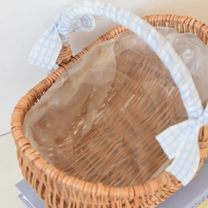 Close-up of handmade wicker picnic basket featuring a blue checkered bow and waterproof liner