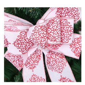 Macro detail of white faux linen Christmas bow with red glitter scrolls on a green tree
