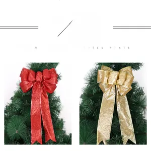 Detail of red and gold Christmas bows with glitter finish hanging on a green pine tree branch
