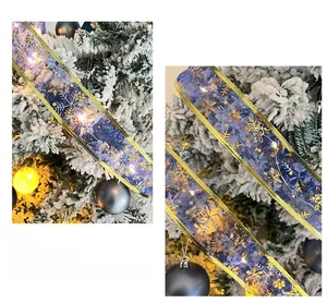 Blue Christmas ribbon with gold snowflakes and warm LED lights on a snowy tree