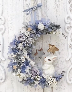Detail of moon-shaped Christmas wreath with blue faux roses and white ceramic rabbit