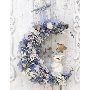 Moon shaped Christmas wreath with blue roses, white rabbit and wooden stars on white door