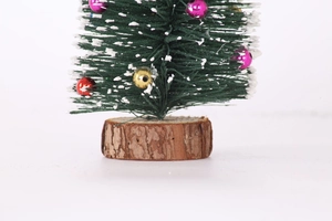 Mini-Weihnachtsbaum mit weißer Beflockung und bunten Kugeln auf einem Holzsockel