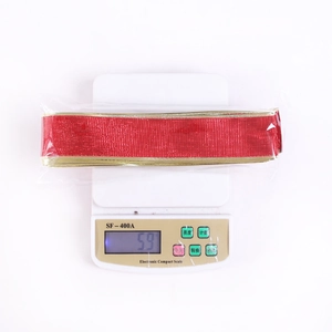 Red Christmas ribbon roll with gold edges weighed on a digital scale for size verification