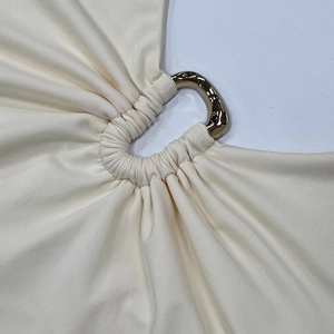 Makro-Detail des cremefarbenen Strickoberteils mit goldenem Ring und Stoffraffungen