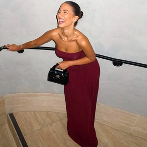 Femme souriante portant une robe longue bustier bordeaux sur un escalier chic