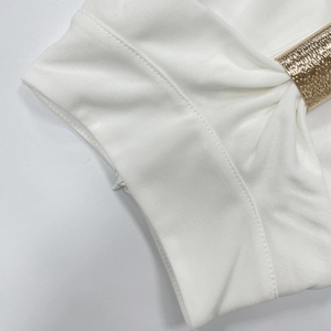 Dettaglio dell'abito bianco con eleganti pieghe in vita e anello in metallo dorato martellato