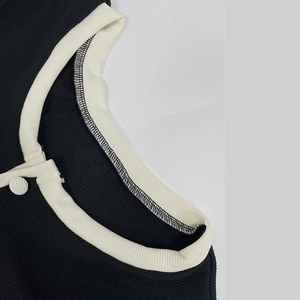 Gros plan du col contrasté sur le body en maille côtelée noire avec bouton décoratif