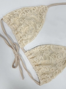 Dettaglio del top bikini in pizzo beige con motivi all'uncinetto e lacci regolabili