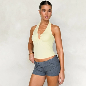 Detail eines gelben Halterneck-Tops mit goldenem Ring und grauen Shorts mit tiefem Bund
