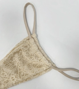 Dettaglio di un abito in pizzo beige con ricami floreali e spalline sottili sul collo