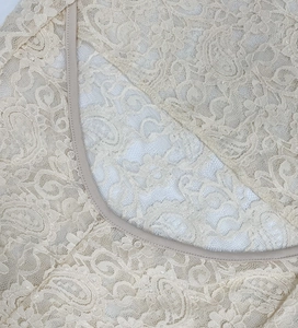 Dettaglio vestito in pizzo beige con motivi floreali paisley e finiture delicate sui bordi