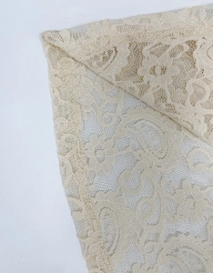 Primo piano del tessuto in pizzo bianco crema con motivi floreali traforati e cuciture pulite