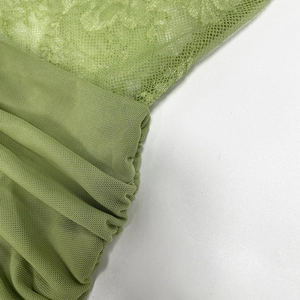 Macro shot of green mesh fabric with detailed lace embroidery and semi-transparent texture