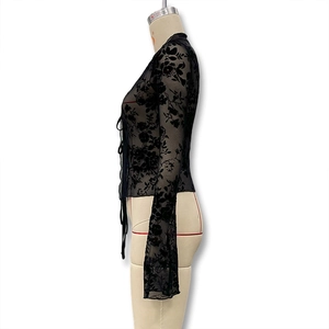 Detail of sheer black floral lace mesh top featuring flared bell sleeves and front tie closure