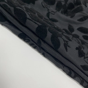 Close-up of black mesh fabric with leaf-shaped flocked patterns and textured finish