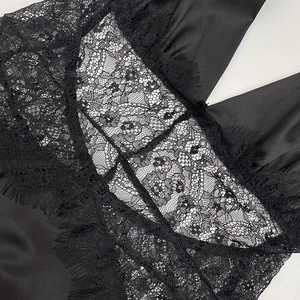 Close-up of elegant eyelash lace trim and smooth satin fabric on a deep V-neck black dress
