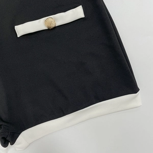 Détail du combishort en maille noire avec bordure blanche et bouton doré sur la poche