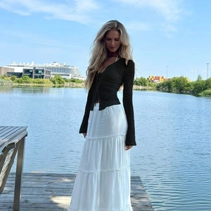 Detail of sheer black lace cardigan and tiered white skirt worn by a model by the lake