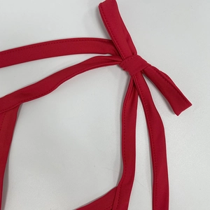 Detail of red halter dress featuring textured elastic fabric and tied bow strap design
