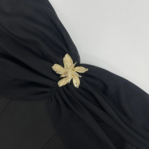 Dettaglio di una spilla a fiore dorata vintage fissata sul tessuto a rete nero dell'abito