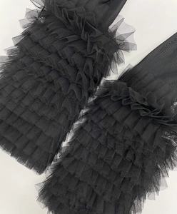 Detail of black tiered mesh leg warmers with layered ruffle design and sheer fabric