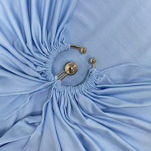 Détail du tissu côtelé bleu clair avec une boucle dorée et des plis élégants sur la robe