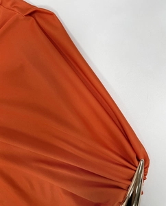 Detailansicht eines orangefarbenen Kleides mit goldener Metallschnalle und Faltenstoff