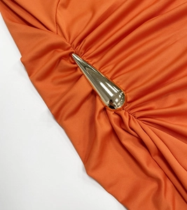 Detail eines orangen Kleides mit dekorativer goldener Metallschließe und Raffung