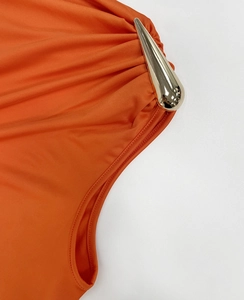Detailansicht eines orangefarbenen Kleides mit goldener Metallschnalle und Falten