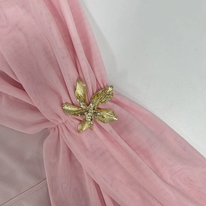 Dettaglio della spilla a fiore in metallo dorato spazzolato su tessuto a rete rosa