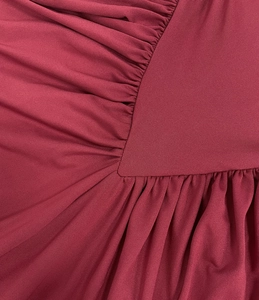 Macro detail of wine red knitted dress showing fine ruching and elegant V-shaped seams