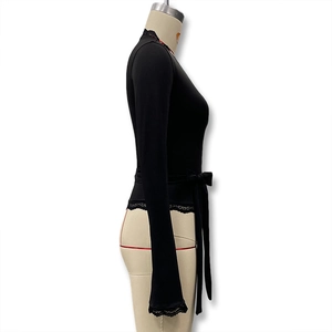 Détail du haut à manches longues avec col en V, dentelle de cils noire et nœud à la taille