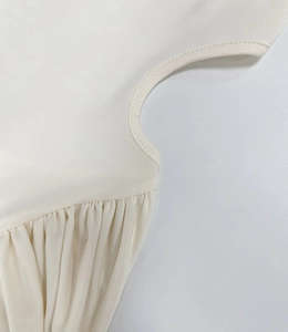 Detailed close-up of beige ruched fabric with fine stitching on a long-sleeve dress