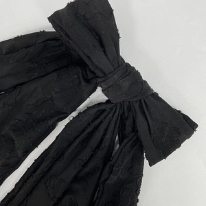 Close-up of black floral jacquard fabric with elegant textured bow detail on the dress