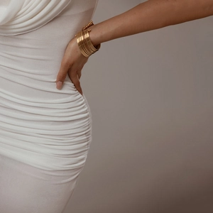 Detail of a multi-layer gold cuff bracelet with metal beads on an elegant white dress