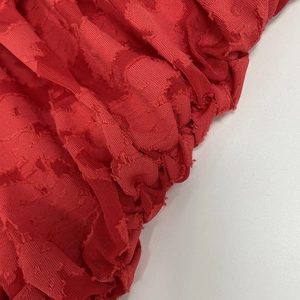 Macro shot of red textured chiffon fabric featuring embossed dot jacquard and draped pleats