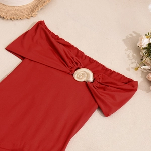 Détail de la robe tricotée rouge à épaules dénudées avec une boucle dorée en forme de coquille