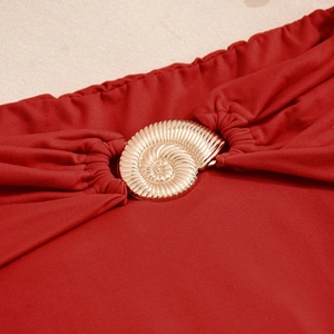 Détail de la boucle coquillage dorée sur le tissu plissé d'une robe rouge